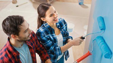 Genç güzel çift Talk ve yeni daire süsleyin. Koca ve karısı açık mavi boya daldırma olan silindirler ile duvar boyama vardır. Onlar mutlu ve gülmek vardır. Evde tadilat.