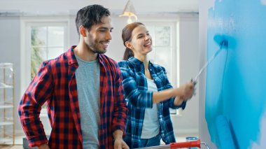 Genç güzel çift Talk ve yeni daire süsleyin. Koca ve karısı açık mavi boya daldırma olan silindirler ile duvar boyama vardır. Evde tadilat.