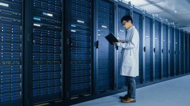 Veri Merkezi: erkek o uzman beyaz ceket giyen sunucu raf yanında standları, bakım tanılama araçları çalıştırmak için dizüstü bilgisayar kullanır, böylece veritabanı En Iyi düzeyde çalışır kontrol.