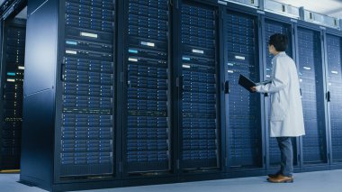 Veri Merkezi: erkek o uzman beyaz ceket giyen sunucu raf yanında standları, bakım tanılama araçları çalıştırmak için dizüstü bilgisayar kullanır, böylece veritabanı En Iyi düzeyde çalışır kontrol.
