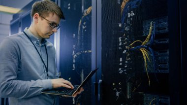 Veri merkezi 'nde çalışan sunucu raf rutin bakım kontrol ve tanılama laptop kullanarak yapmadan önce mühendis standları. Görünür bilgisayar donanım ekipmanları, Broadband fiber optik kablolar LED ışıklar.