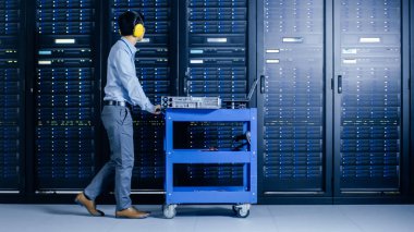Modern veri merkezi: It mühendisi bakım ve tanılama yapıyor. Sunucu rafları ile birlikte sepeti iter, planlanan sistem güncellemesi için yeni donanım yüklemek için kabine açar, ekipman değiştirilmesi.