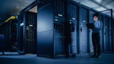 Veri merkezi 'nde: erkek IT teknisyeni çalışan bakım programı bir dizüstü bilgisayar, kontroller operasyonel sunucu raf optimum Işleyişi. Modern High-Tech telekomünikasyon operasyonel süper bilgisayar.