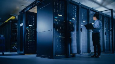 Veri merkezi 'nde: erkek IT teknisyeni çalışan bakım programı bir dizüstü bilgisayar, kontroller operasyonel sunucu raf optimum Işleyişi. Modern High-Tech telekomünikasyon operasyonel süper bilgisayar.