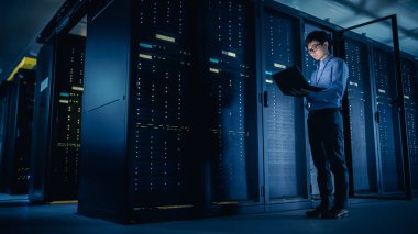 Veri merkezi 'nde: erkek IT teknisyeni çalışan bakım programı bir dizüstü bilgisayar, kontroller operasyonel sunucu raf optimum Işleyişi. Modern High-Tech telekomünikasyon operasyonel süper bilgisayar.