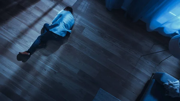 Dålig deprimerad berusad ung man hoppar på golvet nära soffan i en lägenhet med trägolv. Dramatisk ovanifrån kamera Skott. — Stockfoto