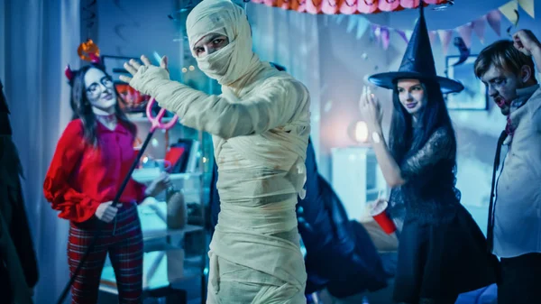 Halloween Costume Party: Old Skinny and Bandaged Mummy Dances (en inglés). En el fondo Zombie, la muerte, la bruja y ella diablo se divierten en una sala decorada fiesta de monstruos —  Fotos de Stock