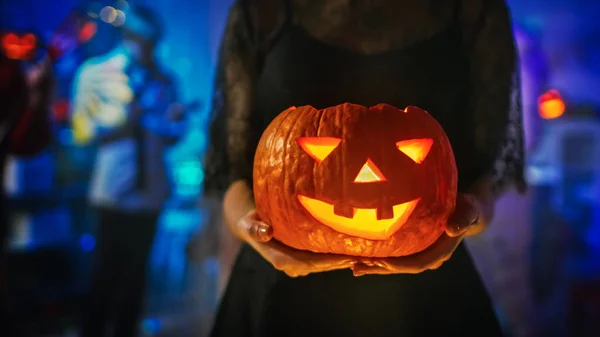 Fiesta de disfraces de Halloween: Precioso vestido de bruja lleva a cabo calabaza ardiente y bailes de manera seductora. Fondo: Hermosa Diablo, Muerte de miedo, Conde Drácula, Zombie bailando en la habitación decorada — Foto de Stock