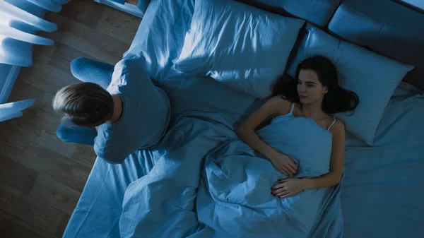 Deprimovaný a stresovaný mladý muž sedí na kraji postele v noci, trpí nespavostí kvůli sexuálním problémům. Jeho mladá žena leží vedle něho cítí se empatie. — Stock fotografie