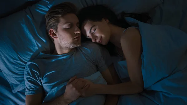 Nejlepší pohled v noci: atraktivní mladý pár spí spolu, drží se v náručí a objímá. První paprsky ranní sluneční osvětlovací místnosti v okně — Stock fotografie