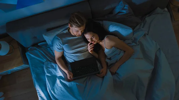 Cuplu drăguț tânăr în pat noaptea folosind laptop, vizionarea seriilor, citirea rețelelor sociale, navigarea prin internet, vorbirea și distracția. Top View Camera Shot — Fotografie, imagine de stoc