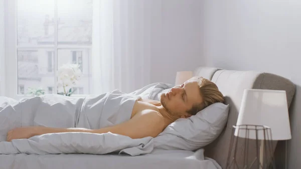 Handsome Fair Boy Lies Cozily in Bed, Opens His Eyes. Depressed Young Caucasian Man. Early Morning Sun Shines Through the Window — Stock Photo, Image