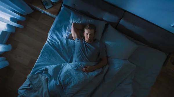 Top View of Handsome Young Man Sleeping Cozily on a Bed in His Bedroom at Night. Blue Nightly Colors with Cold Weak Lamppost Light Shining Through the Window. — Stock Photo, Image