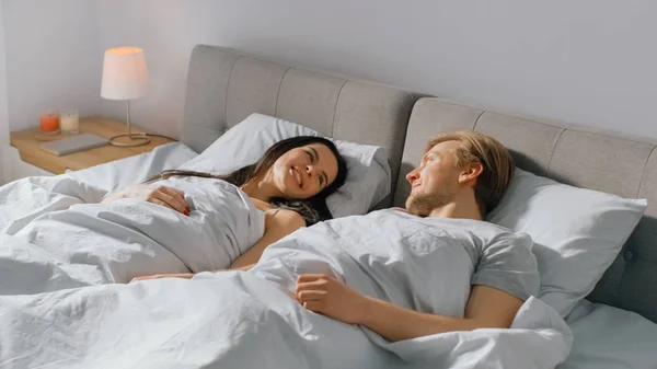 Dimineața soarele răsare și se trezește un cuplu drăguț de tineri în pat, se uită unul la celălalt tandru și zâmbesc. Tineri îndrăgostiți — Fotografie, imagine de stoc