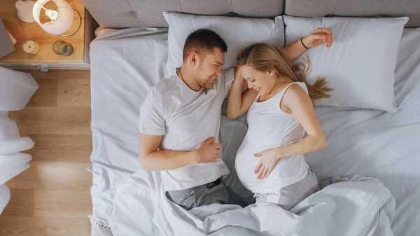 Boldog fiatal pár cuddling együtt az ágyban, fiatal nő terhes és szerető partner érinti, és simogatja Her gyengéden. Top-nézet shot. — Stock Fotó