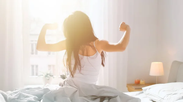 Beautiful Brunette is Waking up in the Morning, Stretches in the Bed, Sun Shines on Her From the Big Window. Happy Young Girl Greets New Day with Warm Sunlight Flare. — Stock Photo, Image