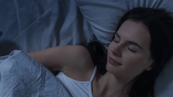 Portrait of Beautiful Young Brunette Charmingly Sleeping in Her Bed at Night in the Dark Room. Sweet and Warm View of Girl Sleeping Calmly. Top Down Shot.