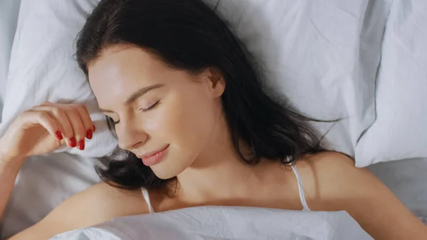 Retrato de la hermosa joven morena que se despierta encantadoramente en su cama y sonríe sensualmente, su rostro está iluminado por el cálido sol de la mañana. Dulce y cálido. Top Down Shot . —  Fotos de Stock