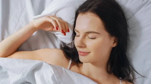 Portrait of Beautiful Young Brunette Charmingly Waking Up in Her Bed and Sensually Smiling, Her Face is Illuminated by the Warm Morning Sun. Sweet and Warm. Top Down Shot. — Stock Photo, Image