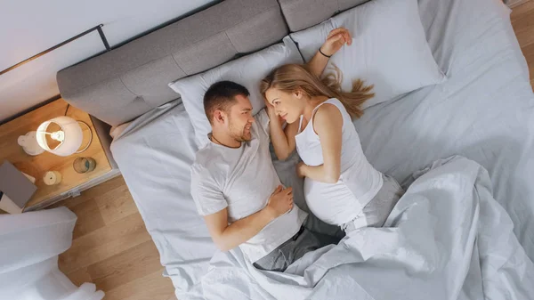 Ευτυχισμένο νεαρό ζευγάρι αγκαλιάζοντας μαζί στο κρεβάτι, νεαρή γυναίκα είναι έγκυος και στοργικά αγγίζει και χαϊδεύει την κοιλιά της τρυφερά. Πλάνο κορυφαίας προβολής. — Φωτογραφία Αρχείου