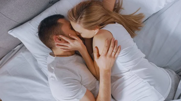 Szczęśliwy młody para cuddling razem w w łóżko, młody kobieta jest w ciąży i kochający partner dotyka i pieszczoty jej brzuch Tenderly, oni pocałunek. Strzał z góry. — Zdjęcie stockowe