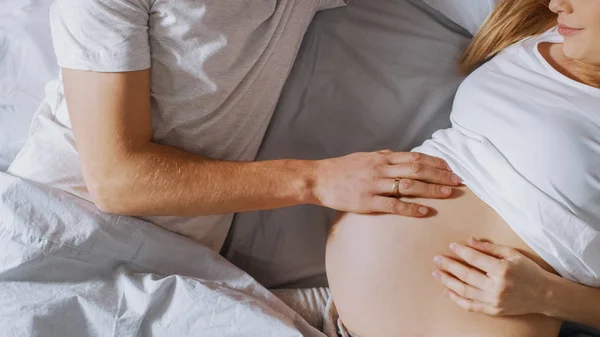 Happy Young Couple Cuddling Together in the Bed, Young Woman is Pregnant and Loving Future Father Touches and Caresses Her Belly Tenderly. Top Down Shot. — Stock Photo, Image