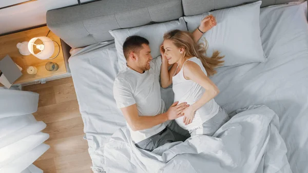 Boldog fiatal pár cuddling együtt az ágyban, fiatal nő terhes és szerető partner érinti, és megcirógatja hasa gyengéden. Top-nézet shot. — Stock Fotó