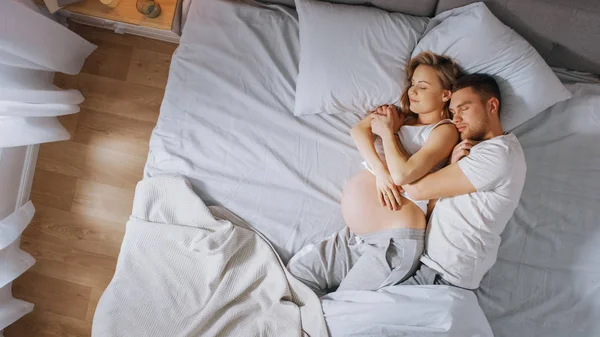 Šťastný mladý pár spí spolu v posteli, sladké milující mladí lidé, kteří se drží při spánku. Krásná žena je těhotná, milující partner ji podporuje tím, že jí. — Stock fotografie