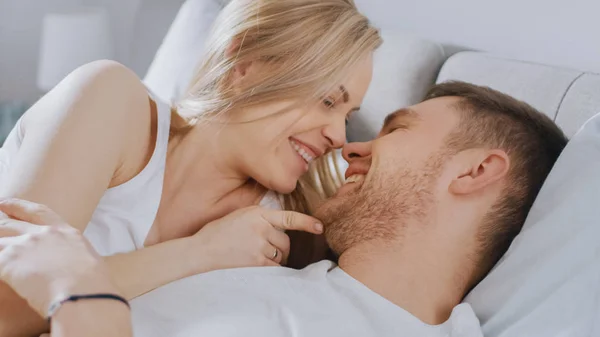 Счастливая молодая пара обнимается в постели, целуется и улыбается. Красивая блондинка и ее крепкий любящий партнер испытывают нежные и любящие моменты совместной жизни . — стоковое фото