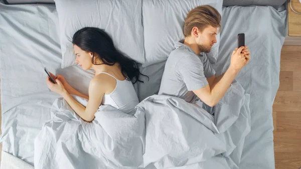Entfremdete junge Millennials im Bett, junge Menschen wenden sich mit Smartphones voneinander ab, surfen in sozialen Netzwerken und reden nicht miteinander. Schuss von oben nach unten. — Stockfoto