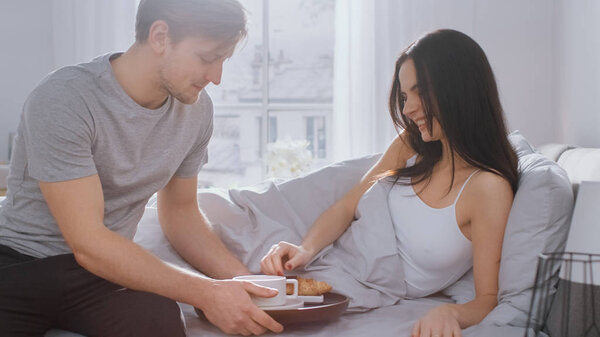 Shot of a Caring Young Man Bringing Tray with Breakfast in Bed to His Lovely Female Partner. Ideal Tender Relationship and Coffee and Croissants in Bed.