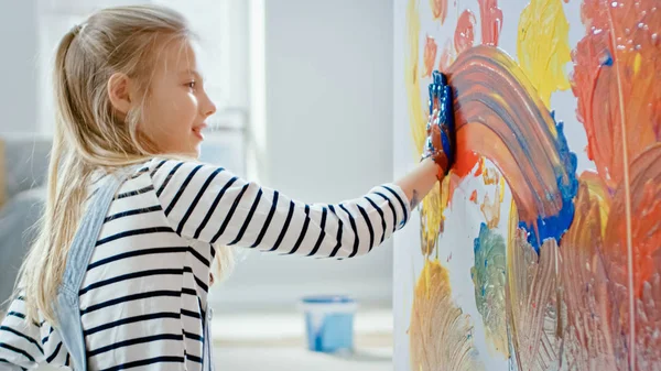 Lycklig liten flicka med händerna doppade i levande färg drar färgglada abstraktioner på väggen. Hon har roligt och skrattar. Hem renoveras. — Stockfoto