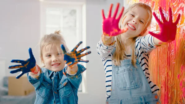 Dos Hermanitas Divertidas Muestran Sus Manos Que Están Sumergidas En Pintura Colorida. Son felices y ríen. Objetivos de Hermandad. Redecoración en casa . —  Fotos de Stock