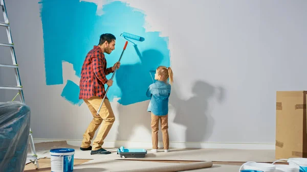 Young far visar hur man målar väggar till söt liten dotter. De målar tillsammans med rullar som är täckta av ljusblå färg. Renovering av rum hemma. — Stockfoto