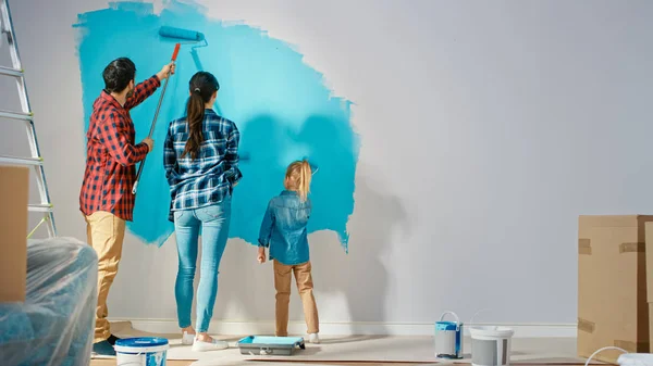 Back Shot of a Young Family Painting Walls with Their Cute Small Daughter (em inglês). Eles pintam com rolos que são cobertos com tinta azul clara. Renovações de quarto em casa . — Fotografia de Stock