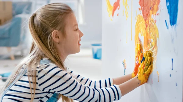 Menina feliz com as mãos mergulhadas na pintura colorida desenha um coração vívido na parede. Ela está se divertindo e rindo. Casa está sendo renovada . — Fotografia de Stock