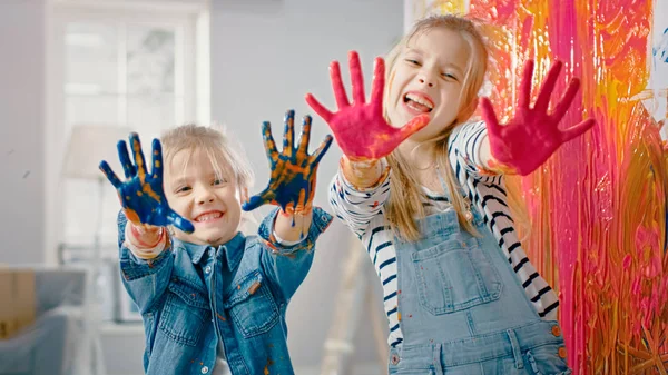 두 재미 작은 자매는 화려한 페인트에 담근 자신의 손을 보여줍니다. 그들은 행복하고 웃습니다. 자매결연 목표. 집에서 재장식. — 스톡 사진