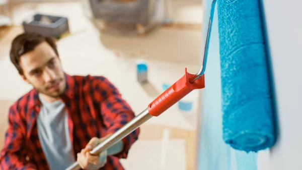 Close-up shot van een man in bruine jeans en rode geruite overhemd schilderij een muur met een roller. Verfkleur is licht blauw. Kamer renovatie thuis. Shot van bovenaf. — Stockfoto