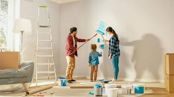 아름다운 젊은 가족은 사랑스러운 작은 딸에게 벽을 칠하는 방법을 보여주고 있다. 그들은 밝은 파란색 페인트로 덮여 롤러로 페인트. 홈 객실 리노베이션. — 스톡 사진
