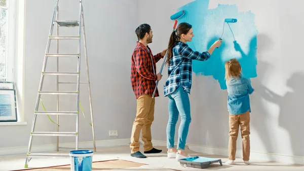 Familie tijd samen met kleine dochter. Jonge vader en moeder tonen hun kind hoe een muur te schilderen met een roller. Verfkleur is licht blauw. De kamer in huis is voorbereid op renovatie. — Stockfoto