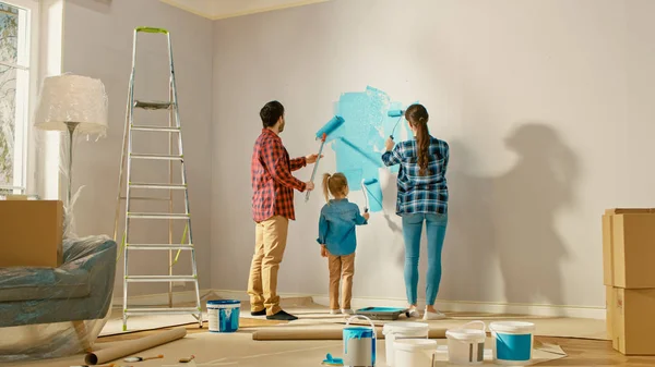 Familie tijd samen met kleine dochter. Jonge vader en moeder tonen hun kind hoe een muur te schilderen met een roller. Verfkleur is licht blauw. De kamer in huis is voorbereid op renovatie. — Stockfoto