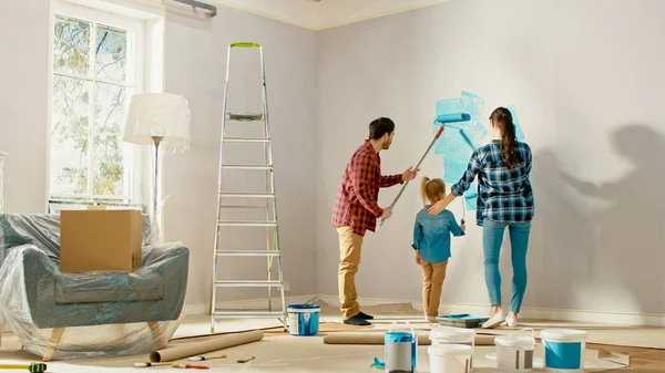 Die schöne junge Familie zeigt ihrer entzückenden kleinen Tochter, wie man Wände bemalt. Sie malen mit Rollen, die mit hellblauer Farbe überzogen sind. Renovierungen zu Hause. — Stockfoto