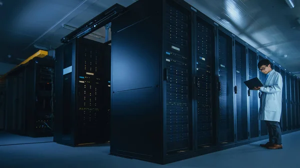 A Data Center: férfi it Specialist visel fehér kabát állványok mellett Server rack, használ laptop számítógép-hoz fuss karbantartás diagnosztikai eszközök, ellenőrzések, hogy az adatbázis működik az optimális szinten. — Stock Fotó