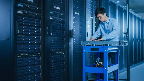 En el centro de datos moderno: Técnico de TI que trabaja con bastidores de servidores, en un carrito Se necesitan varios equipos para instalar nuevos discos duros, hacer mantenimiento y diagnóstico de hardware . —  Fotos de Stock