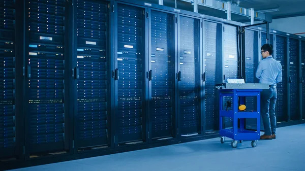 In Data Center: Male IT Technician Running Maintenance Programme on a Laptop, Controls Operational Server Rack Optimal Functioning. Modern High-Tech Telecommunications Operational Super Computer. — Stock Photo, Image