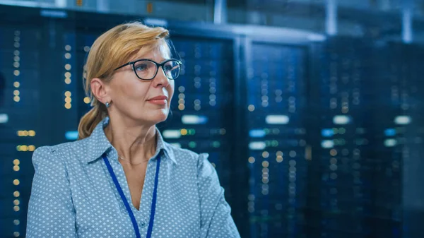 Retrato de una hermosa mujer mayor Técnico de TI de pie en el centro de datos moderno. En los bastidores del servidor de trabajo de fondo con luces led parpadeantes . — Foto de Stock