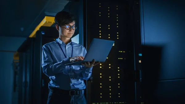 In Dark Data Center: Specialista IT maschile si trova accanto alla fila di rack server operativi, utilizza il computer portatile per la manutenzione. Concetto per Cloud Computing, Intelligenza Artificiale, Supercomputer, Cybersecurity. Luci al neon — Foto Stock