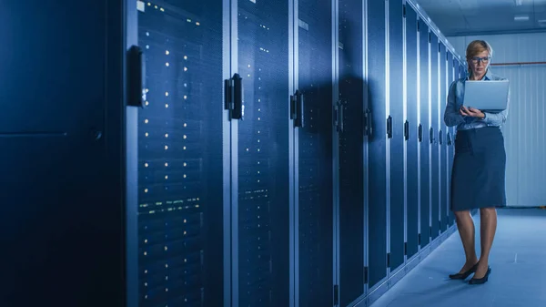 In Data Center: vrouwelijke IT-technicus met onderhoudsprogramma op een laptop, regelt de operationele server rack optimale werking. Moderne high-tech telecommunicatie operationele super computer. — Stockfoto