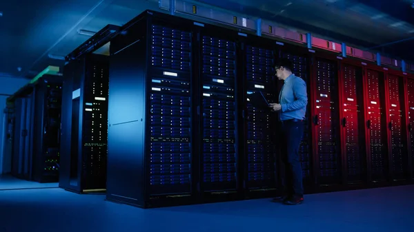 I Data Center: manliga IT-specialist går längs raden av operativa Server rack, använder laptop för underhåll. Koncept för telekommunikation, Cloud Computing, artificiell intelligens, superdator — Stockfoto