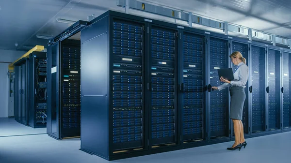 In Data Center: vrouwelijke IT-technicus opent de rack kast en voert een onderhoudsprogramma uit op de laptop, regelt de optimale werking van de operationele server. — Stockfoto